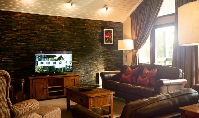 Lounge area interior of the three bedroom lodge, with brown leather sofas and a TV sitting on top of a wooden TV unit.