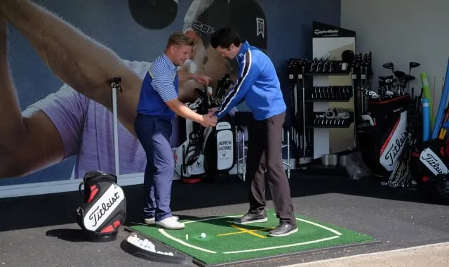 a man helping another man hold his club to practice his golf swing