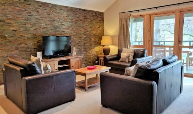 Lounge area of one bedroom lodge, with leather seating around a coffee table, with greenery visible through the window.