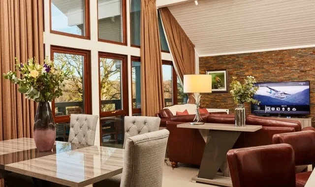 A modern seating area with a dining table and chairs, with Loch Lomond visible through arched windows.