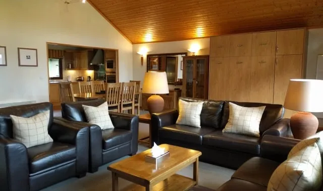 Interior of the two bedroom lodge, featuring black leather sofa around a brown wooden table.