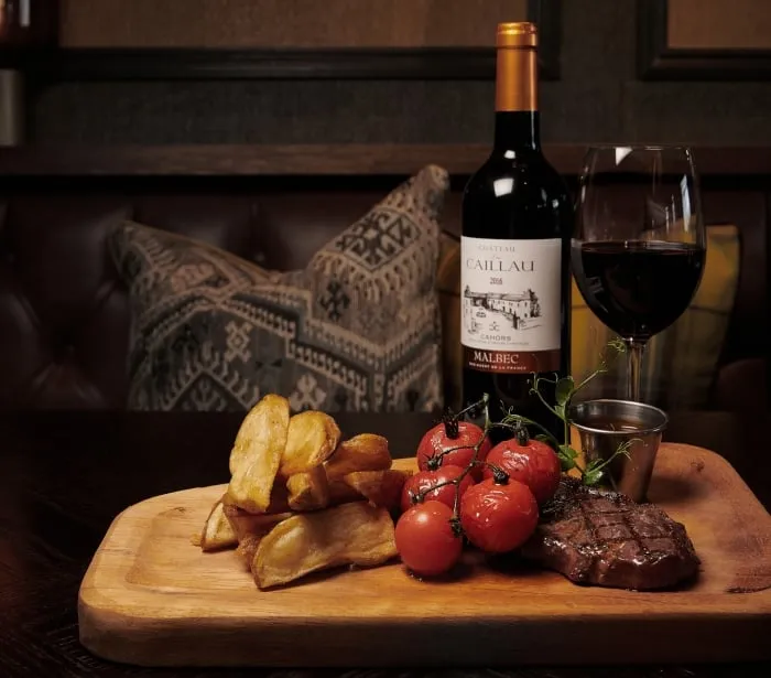a board with steak, tomatoes, potatoes and red wine