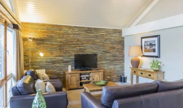 Living area with a large window and brick wall, featuring a brown sofa facing a TV unit.