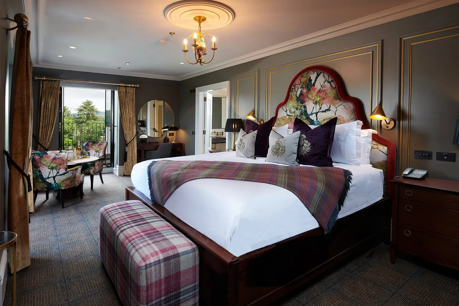 a large floral pattern bed with floral chairs surrounding a table and a door way to a patio