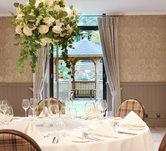 white table with chairs surrounding it and a large white floral arrangement and a gazebo outside an open door
