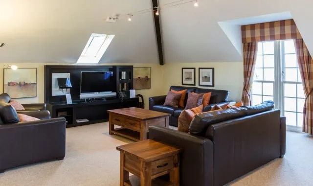 Spacious living area inside a four-coach lodge at Cameron Lodges, featuring leather sofas, wooden furnishings and skylights, one of the luxury Loch Lomond lodges.