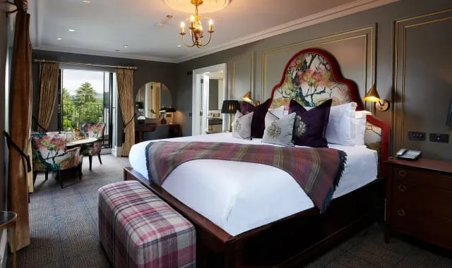 a large floral pattern bed with floral chairs surrounding a table and a door way to a patio