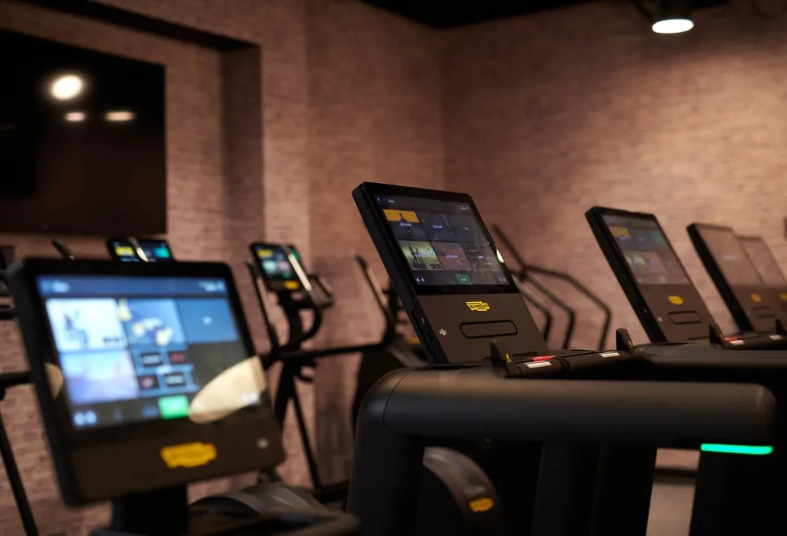 close up view of screens on treadmills with other cardio equipment in the back