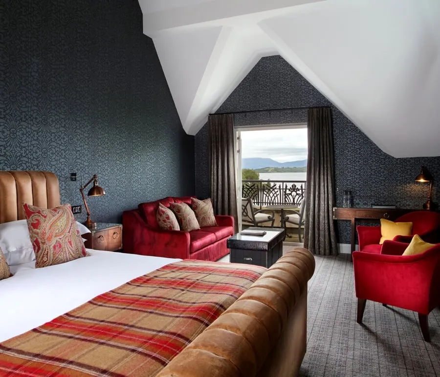 a bed sitting in a bed room with a red couch and two red chairs in front of a patio sitting area